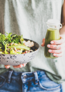 A woman holding a salad and green juice
